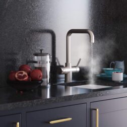 A black modern kitchen design with a stylish D-shape brushed nickel hot water tap dispensing streaming water over a white sink