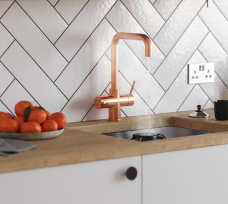 A D-shape copper finish instant boiling tap streaming hot water into a black cup