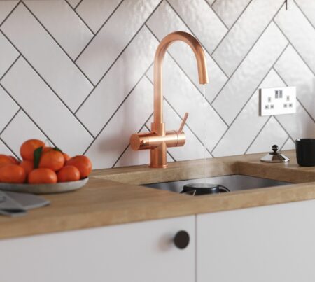 A copper swan neck tap in a wooden-style kitchen countertop dispensing boiling water into a mug