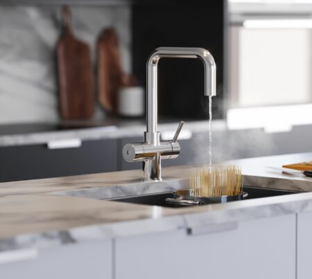 A D-shape water tap in chrome runs hot water over uncooked pasta in a pot