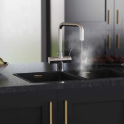 a D-shape brushed nickel boiling water tap streaming hot water into a modern black kitchen countertop sink