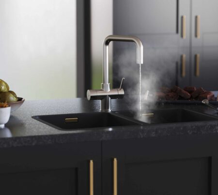 a D-shape brushed nickel boiling water tap streaming hot water into a modern black kitchen countertop sink