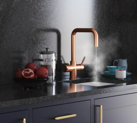 a D-shape copper boiling water tap streaming hot water into a modern black kitchen countertop