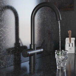 A swan neck hot water tap in matt black pours water into a crystal glass