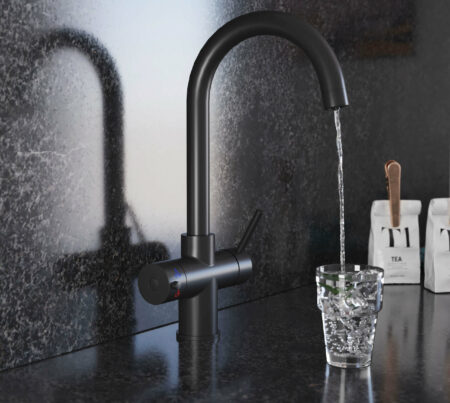 A swan neck hot water tap in matt black pours water into a crystal glass