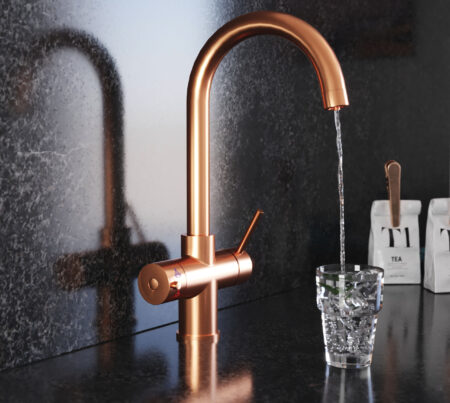 A swan neck hot water tap in copper pours water into a clear glass