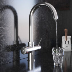 A swan neck hot water tap in chrome pours water into a crystal glass