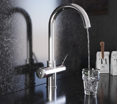 A swan neck hot water tap in chrome pours water into a crystal glass