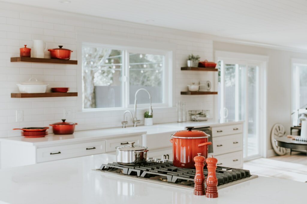 a well-lit white kitchen with flame orange utensils, a brushed nickel swan neck tap beside a big white sliding window