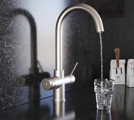 A swan neck hot water tap in brushed nickel pours water into a crystal glass