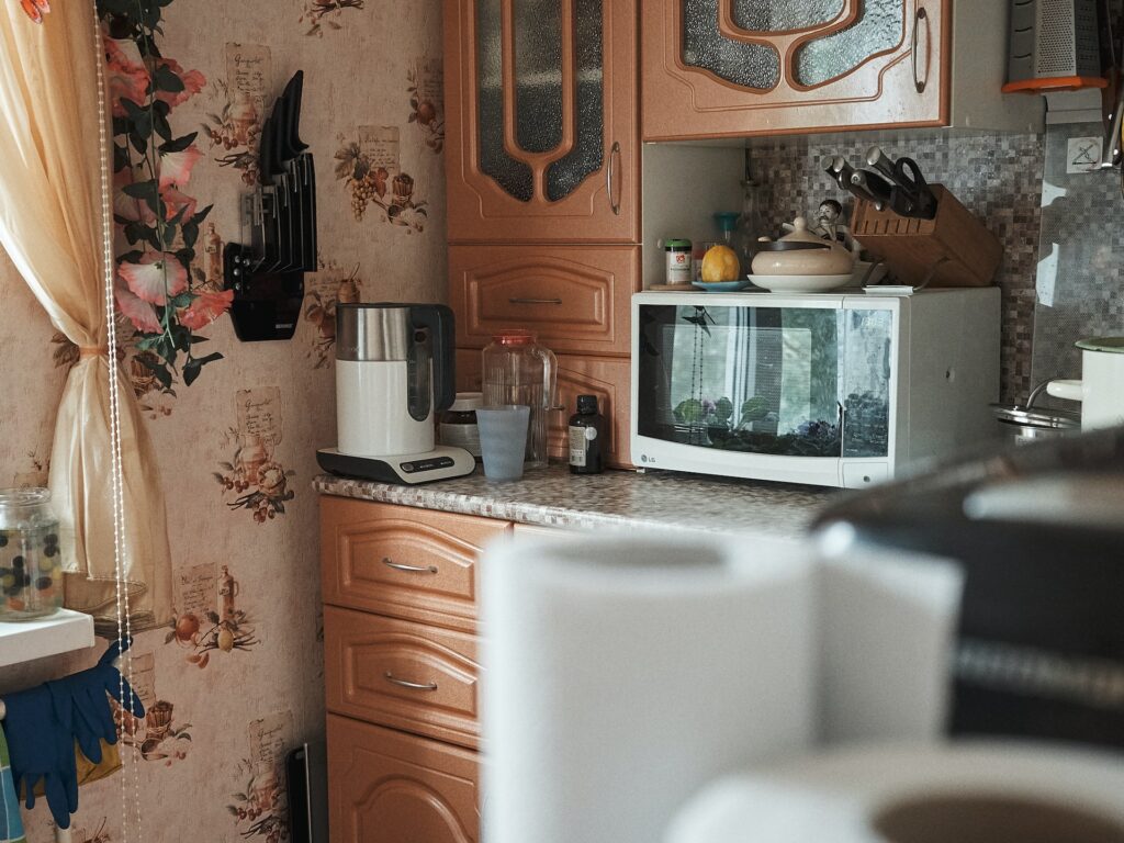 wooden brown kitchen cabinets with small square tile countertop matching with a light brown printed wallpaper and kitchen utilities