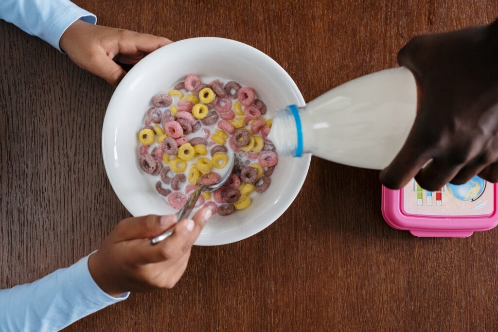 a person pouring milk onto a bowl of cereal