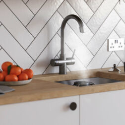 A wooden countertop with a bowl of oranges and a swan neck gunmetal grey instant boiling tap pouring water into a kettle