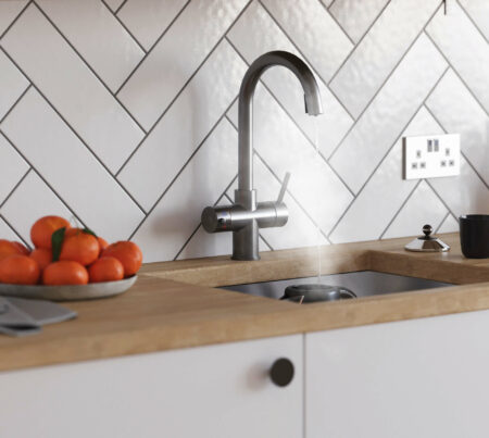 A wooden countertop with a bowl of oranges and a swan neck gunmetal grey instant boiling tap pouring water into a kettle