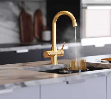 A gold swan neck tap in a modern kitchen dispensing boiling water into a pan of pasta