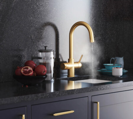 A gold boiling water tap with swan neck running steaming water in dark modern kitchen