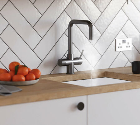 a gun metal D-neck tap running steaming water in a bright kitchen with wooden worktops