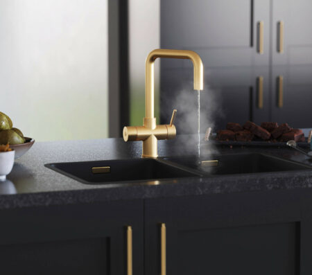 A gold hot water D-neck tap running steaming water in a modern kitchen with black cabinets