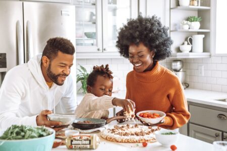 a child beside her parents helps cook on a kitchen table