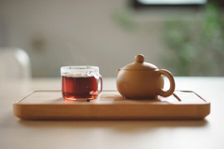 a clear glass cup with tea near a brown ceramic teapot