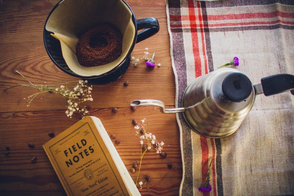 kettle on wooden table with book and filter coffee grounds